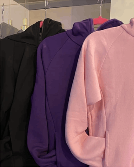 Three Hoodies—black, purple, and light pink—hang side by side on pink hangers in a closet, displaying their fronts and sleeves.